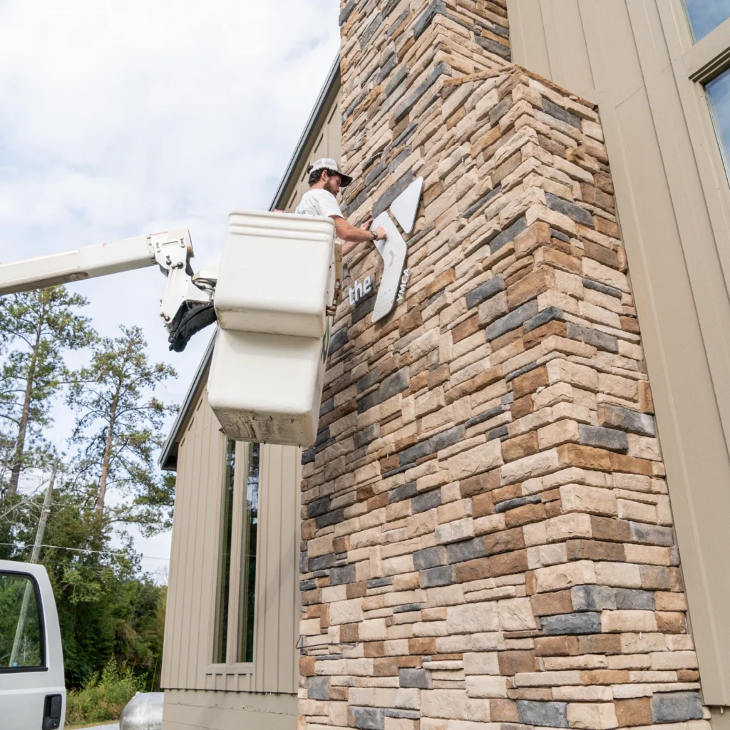 A man in a bucket truck installing an exterior sign of the YMCA logo