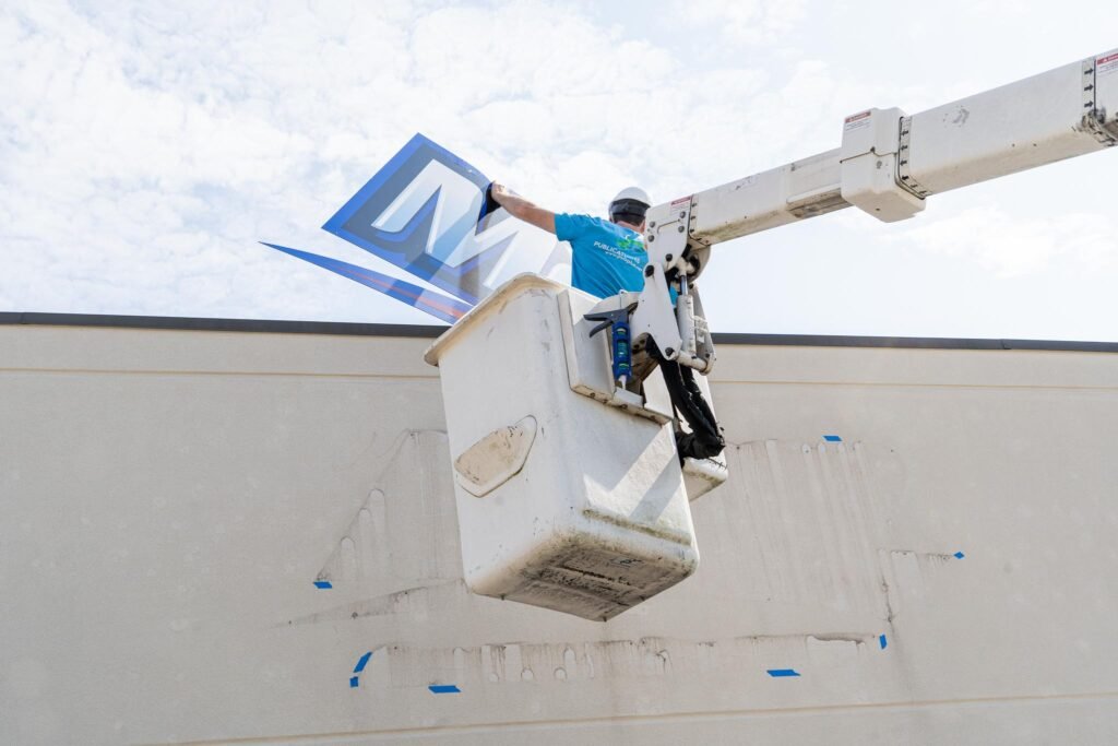 A man in a bucket truck is installing a new sign on the exterior of the building.