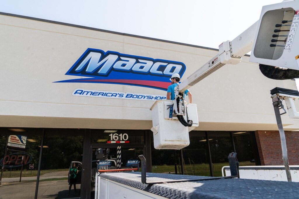 A man in a bucket truck and a new sign on the exterior of a building.