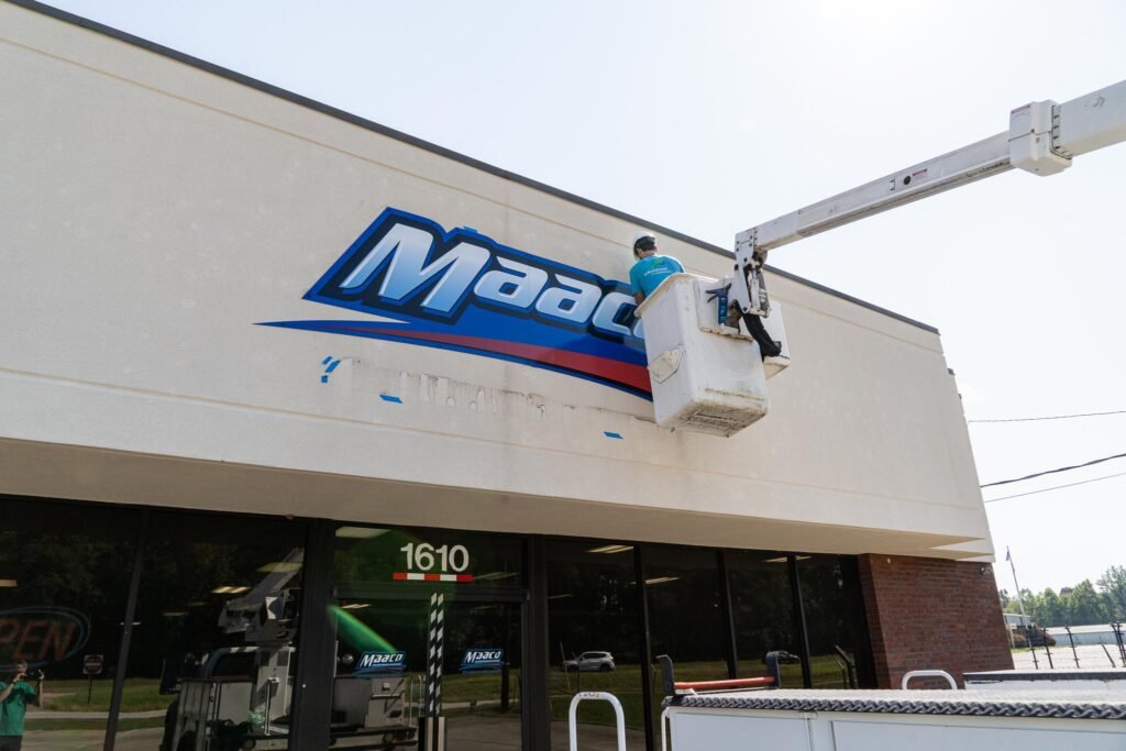 A man in a bucket truck is installing a new sign on the exterior of the building.