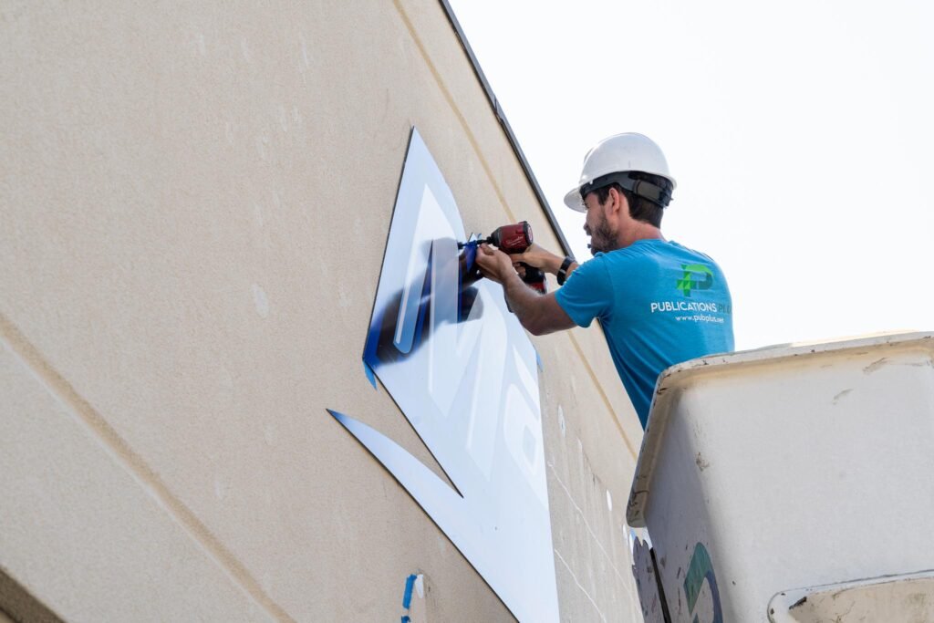 A man in a bucket truck is installing a new sign on the exterior of the building.